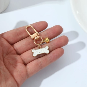Close-up of golden dog bone pendant and small bell on a metal keychain held in hand