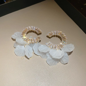 Detail of C-shaped metal earrings with rectangular crystals and white flower petals