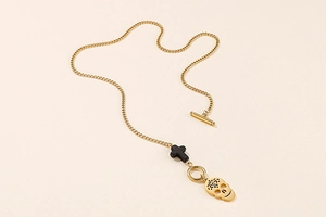 Detail of gold punk necklace with skull pendant, black cross bead and OT toggle clasp