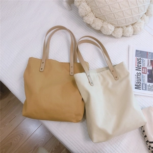 Flat lay of mustard yellow and beige canvas tote bags with leather handles and metal rivets