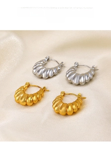 Macro shot of gold and silver chunky wave earrings on soft cream satin fabric