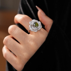 Close-up of a floral silver ring featuring a green oval gemstone and micro-set zircons