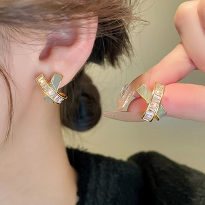 Elegant gold-plated X-cross earrings with inlaid zircons shown on a model's ear