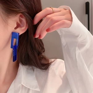 Close-up of deep blue geometric rectangular earrings worn by a model in white shirt