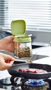 Action shot of glass seasoning jar with green lid pouring salt into a pan