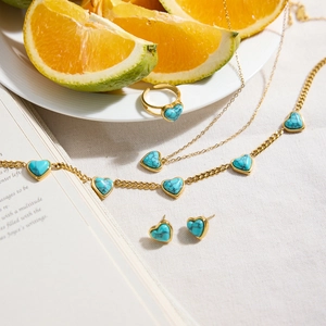 Vue à plat de bijoux coeur turquoise dorés avec orange et livre sur tissu beige