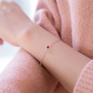 Detail of a thin silver bracelet with a small red heart pendant on a wrist