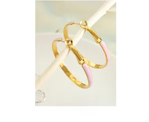 Detail of pink enamel dripping on large gold hoop earrings hanging on white branches