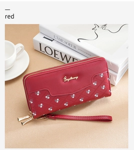 Detail of red long wallet with floral embroidery and dual zippers on a desk