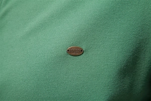 Close-up of a bronze metal badge on green textured pique polo shirt fabric
