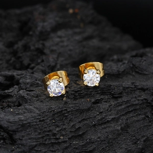 Macro shot of gold-plated round zircon earrings with 4-prong setting on dark stone