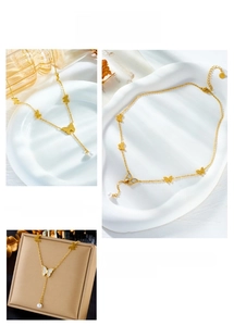 Detail of gold butterfly necklace with white enamel inlays and a hanging pearl drop pendant