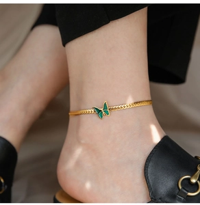 Close-up of gold plated anklet with green butterfly charm on woman ankle