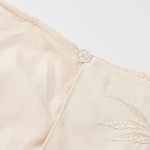 Gros plan détaillé sur tissu beige avec broderie de feuilles et bouton blanc