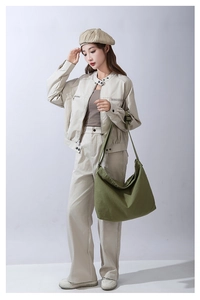 Dettaglio di una grande borsa a tracolla in tela verde con un outfit beige