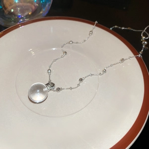 Detail of silver beaded chain necklace with clear crystal ball pendant on a porcelain plate