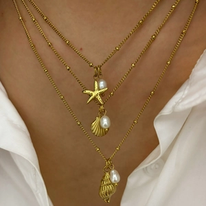 Gold layered necklace featuring starfish and shell pendants with pearls on a white shirt