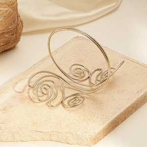 Detail of a golden twisted metal arm cuff with spiral textures on a stone surface