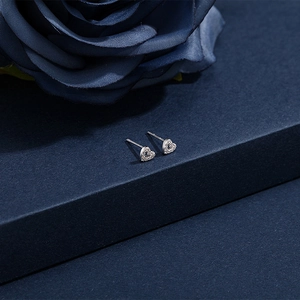 Macro detail of silver heart stud earrings with cubic zirconia on deep blue background