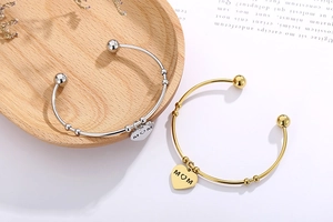 Détail macro de bracelets en or et argent avec gravure MOM sur un plateau en bois
