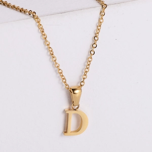 Macro detail of polished 18k gold letter D pendant on a minimalist stainless steel chain