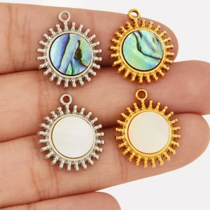 Macro shot of sun pendant charms in gold and silver finish with natural shell inlay