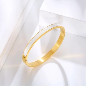 Detail view of a gold-plated stainless steel bangle with white enamel inlay on a white stand