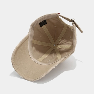 Detailed view of 100% cotton label and metal buckle on a beige distressed baseball cap