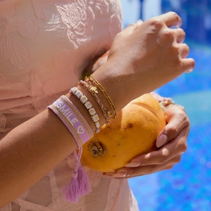 Detail of layered smile embroidery and sister bead bracelets with gold chain by the pool