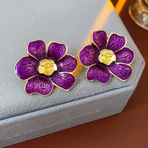 Primer plano detallado de pendientes de flor esmaltada morada con centro dorado en terciopelo