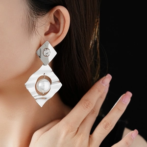 Macro shot of silver rhombic earrings with large floating pearls and wavy metal texture