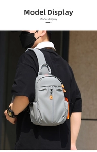 Detail view of a light grey crossbody chest bag with vibrant orange zipper pulls on model