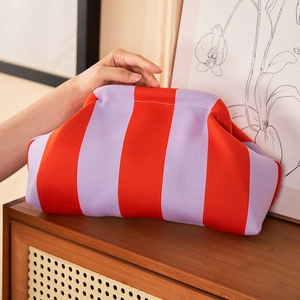 Chic red and purple striped knit cloud clutch bag on a minimalist wooden cabinet