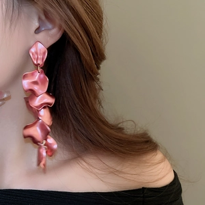 Detailed view of pink metallic petal tassel earrings worn by a model in soft warm lighting