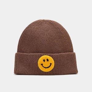 Détail d'un bonnet en tricot marron avec un patch sourire jaune sur le bord replié
