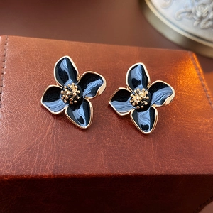 Détail de boucles d'oreilles fleur à quatre pétales avec émail noir et bordure dorée