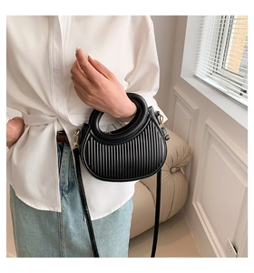 Detail of black saddle bag with vertical pleated texture and golden metal hardware
