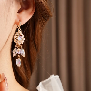 Detail view of gold teardrop heart fringe earrings with crystals on a female model