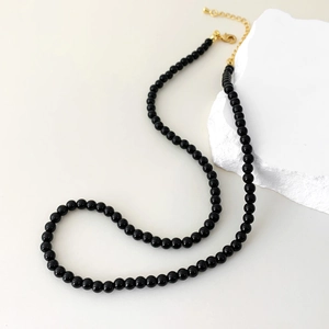 Detail view of black agate beaded necklace with gold lobster clasp on stone prop