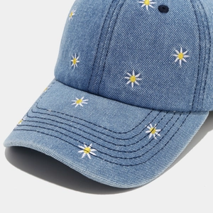 Close-up of blue denim baseball cap featuring detailed white and yellow daisy embroidery