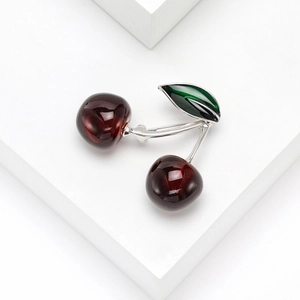 Elegant red cherry brooch with silver metal stem and green enamel leaves on white background