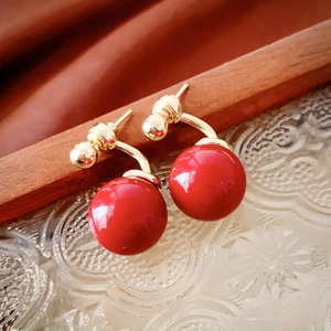 Detailed view of red glossy sphere earrings with gold metal connection on glass tray