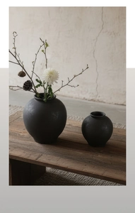 Gros plan de vases minimalistes en céramique noire à texture mate sur un banc en bois