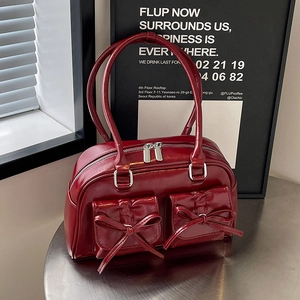 Close-up of shiny dark red shoulder bag featuring 3D bow pockets and silver hardware