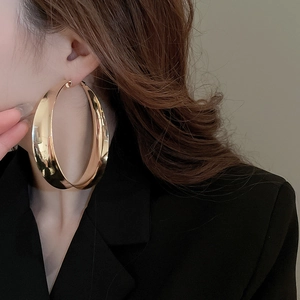 Detailed view of oversized chunky gold hoop earring worn by a model in black attire