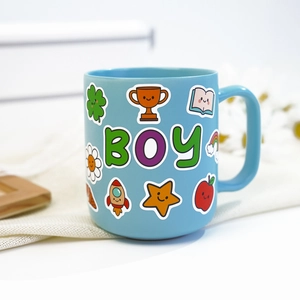Close-up of blue ceramic mug decorated with cute cartoon BOY letters and rocket stickers