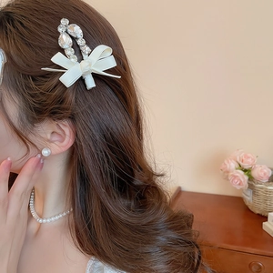 Détail d'une pince à cheveux à nœud en satin blanc avec strass brillants sur un modèle
