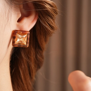 Macro detail of square amber resin earring with crystal inlay worn by a model