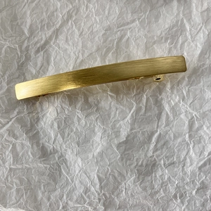 Detailed macro view of long golden metal hair clip with brushed finish texture