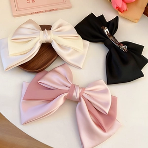 Detail of oversized satin and chiffon bow hair clips in cream, pink, and black colors